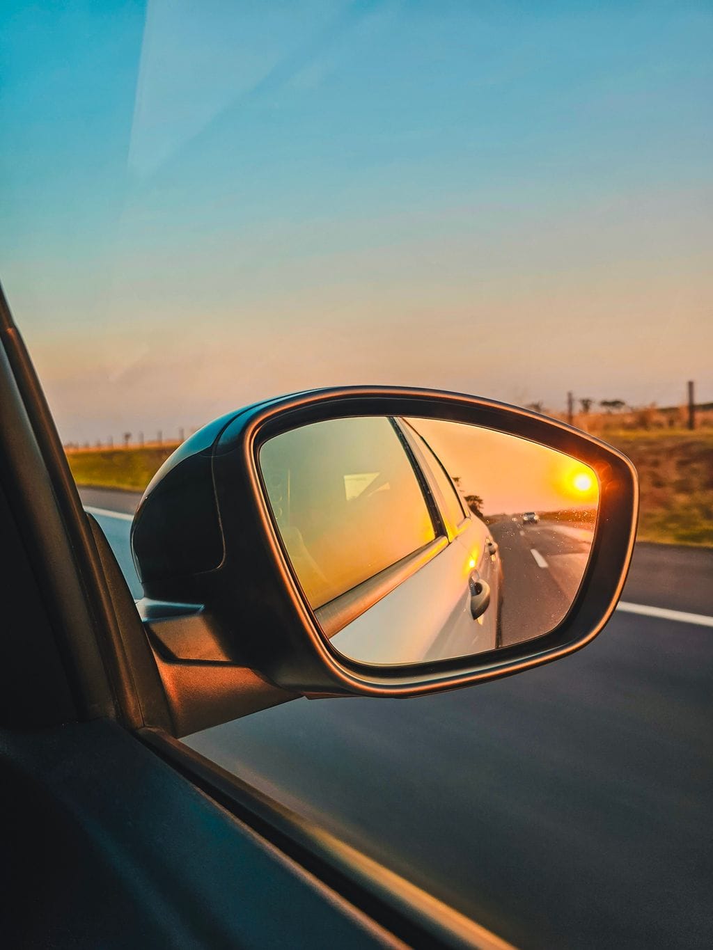 Fotografia da estrada e do pôr do sol refletido no retrovisor do carro